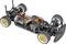 A remote-controlled car chassis with visible cables, motor, and suspension. It has gold alloy wheels and is in a racing configuration.