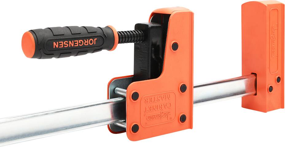 An orange G-clamp with a black handle. It is gripping a piece of metal and is used for holding workpieces in place.