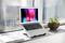 Laptop on windowsill displaying a colourful screen. Plants and notebook beside it. Modern, bright workspace.