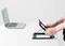 A person is positioning a black laptop stand on a white table, next to an open laptop.