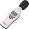 A white sound level meter displays a reading of 57.7 dB. It has a display and several buttons on the front.