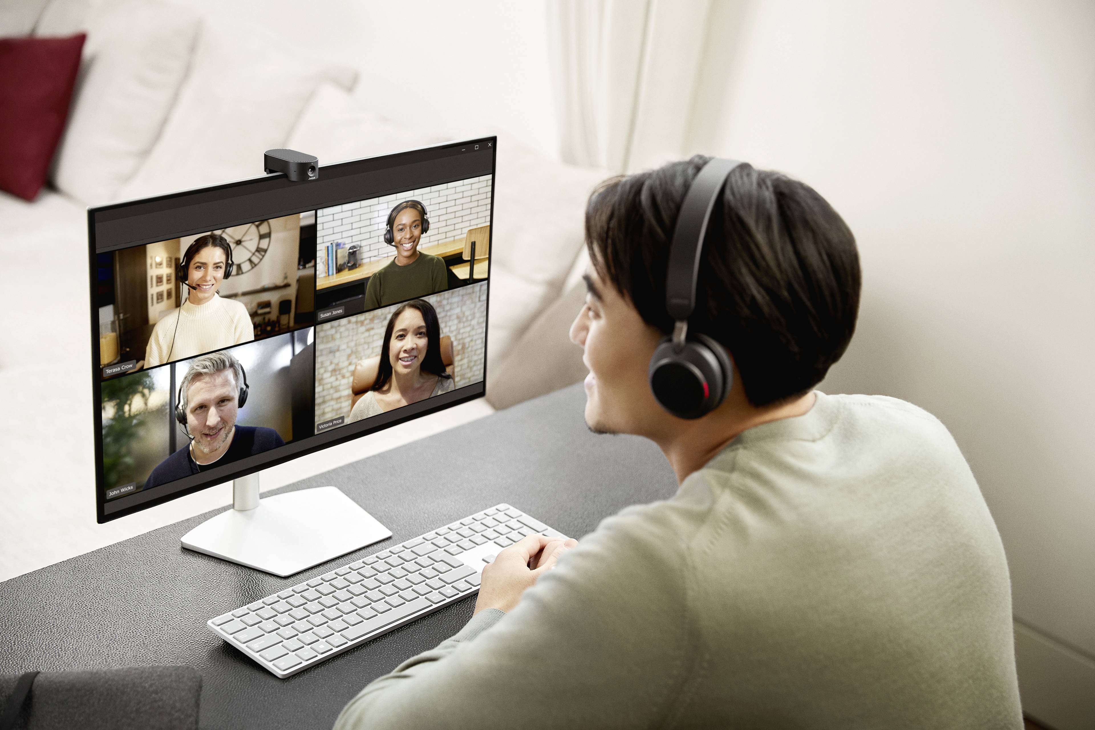 A person in a video call with four other participants on a computer screen. Everyone is wearing headphones and smiling.