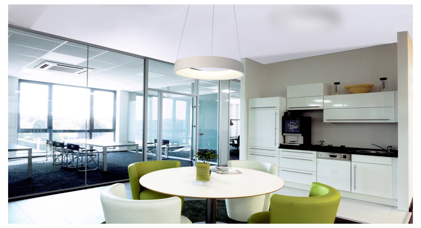 Modern open-plan office kitchenette with round table and chairs beside a glass-walled meeting room and work area.