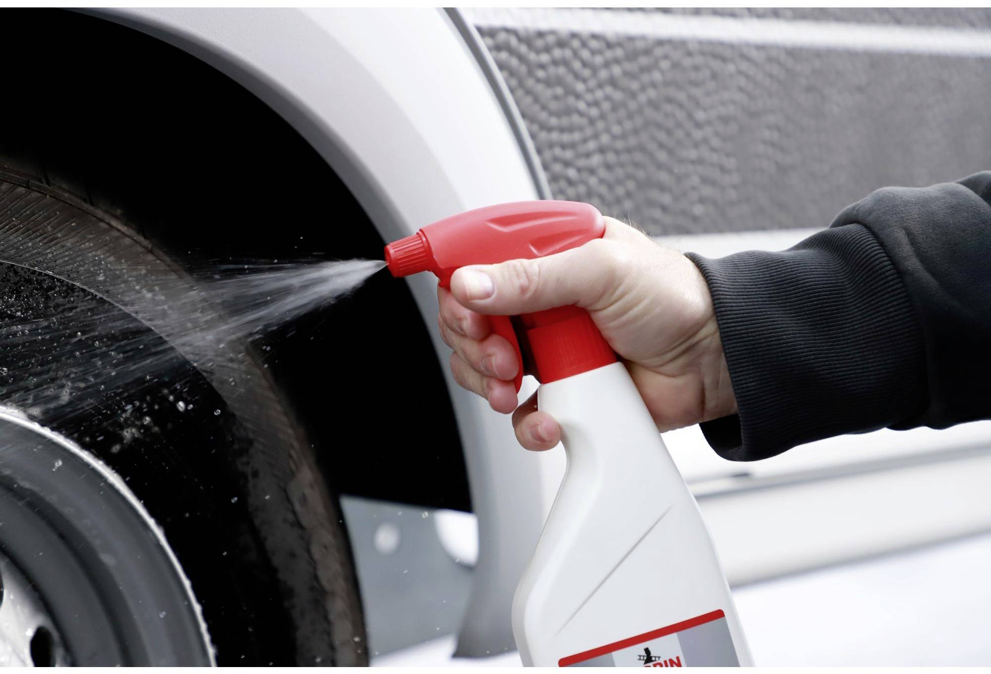 A hand is holding a spray bottle and spraying liquid onto a car tyre to clean the wheel.
