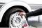 A hand sprays a cleaning product onto a dirty car tyre. The cleaner generates white foam on the wheel rim.