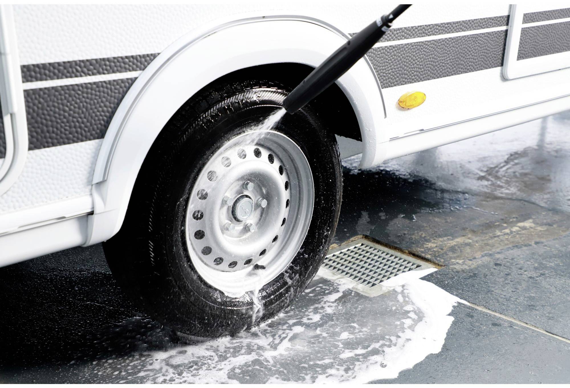 A caravan tyre is being washed with a pressure washer, with soapy water running down the drain.