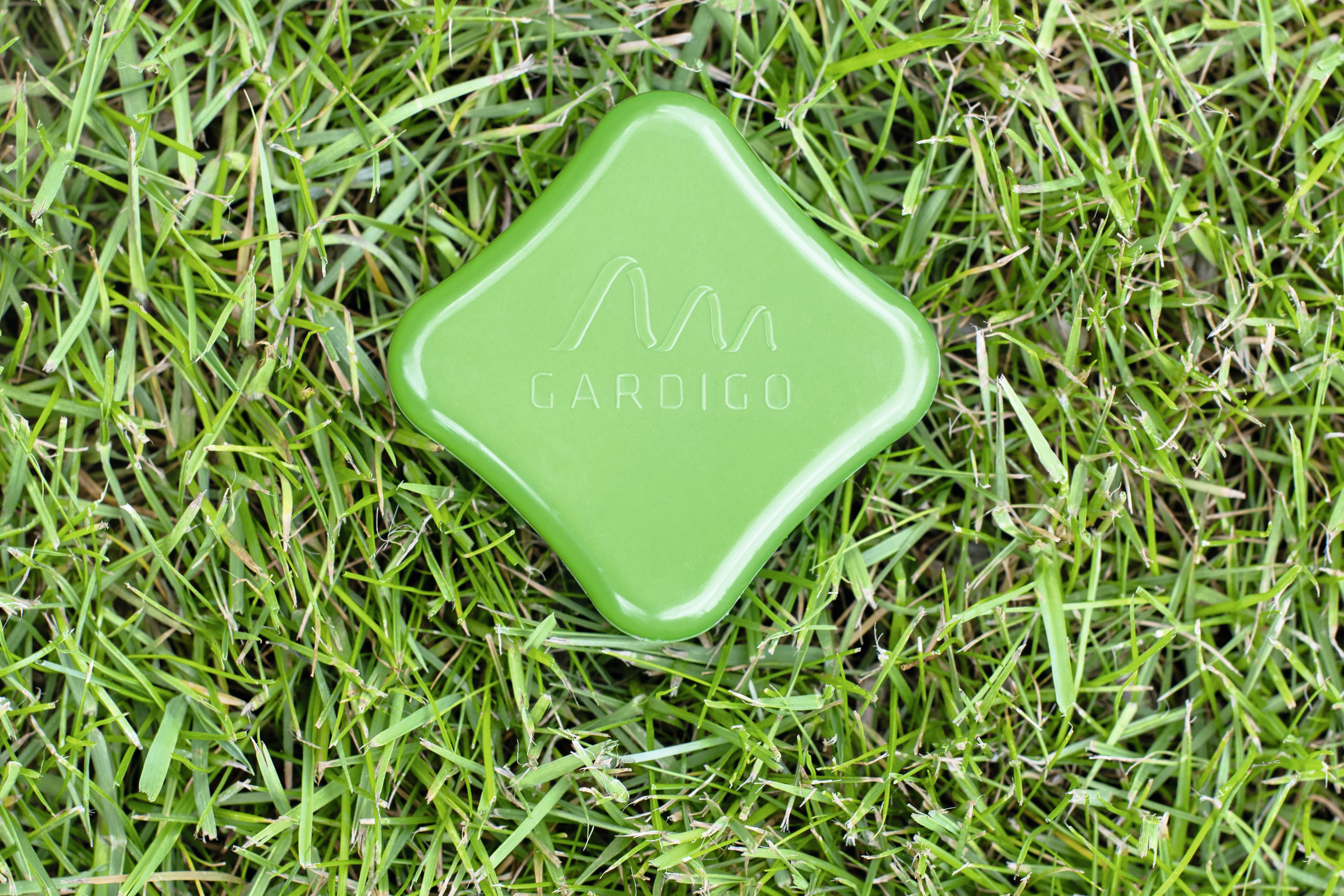 A green electronic device for animal deterrence lies on grass-covered ground.