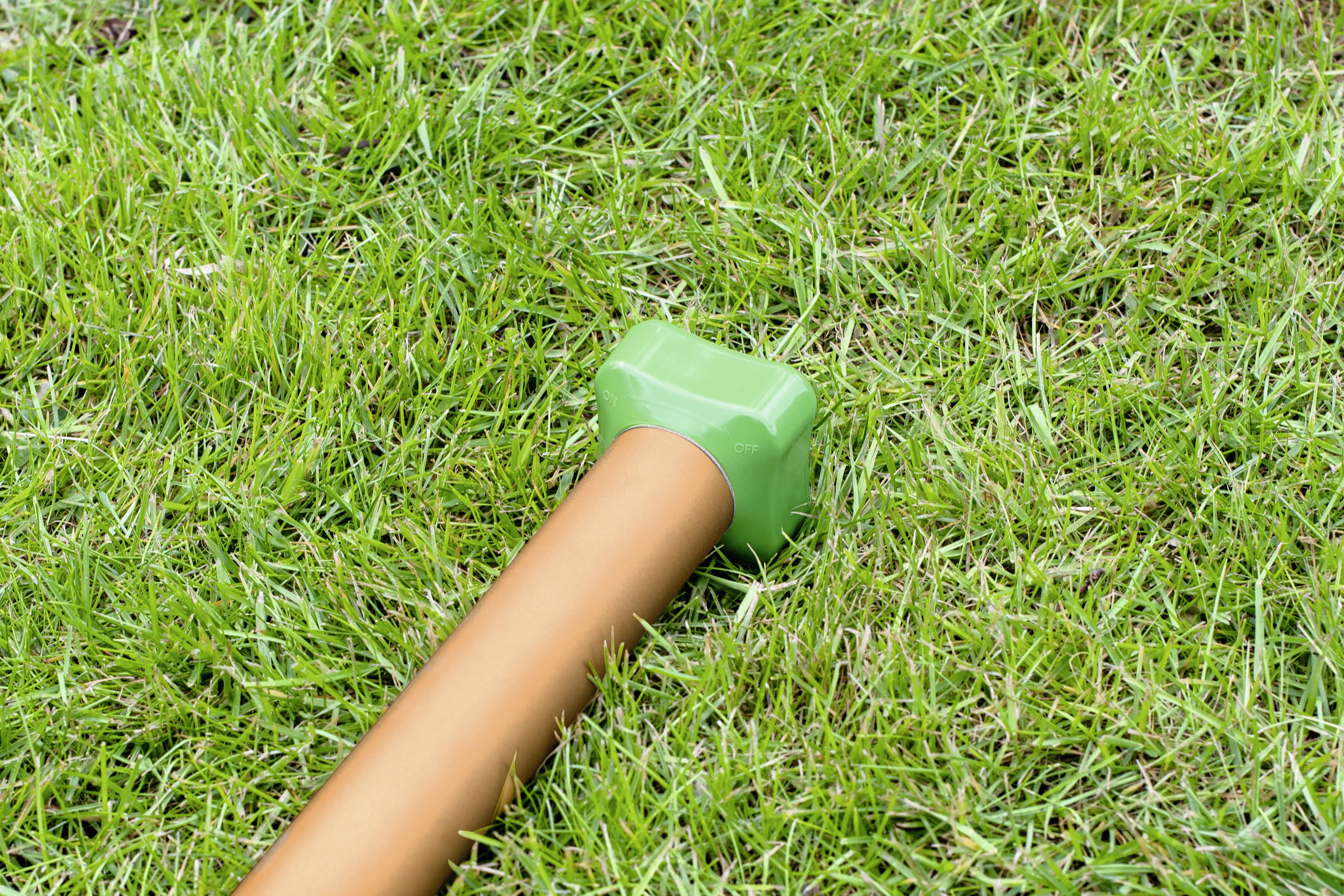 A metal pipe with a green lid lies diagonally on a grassy area.