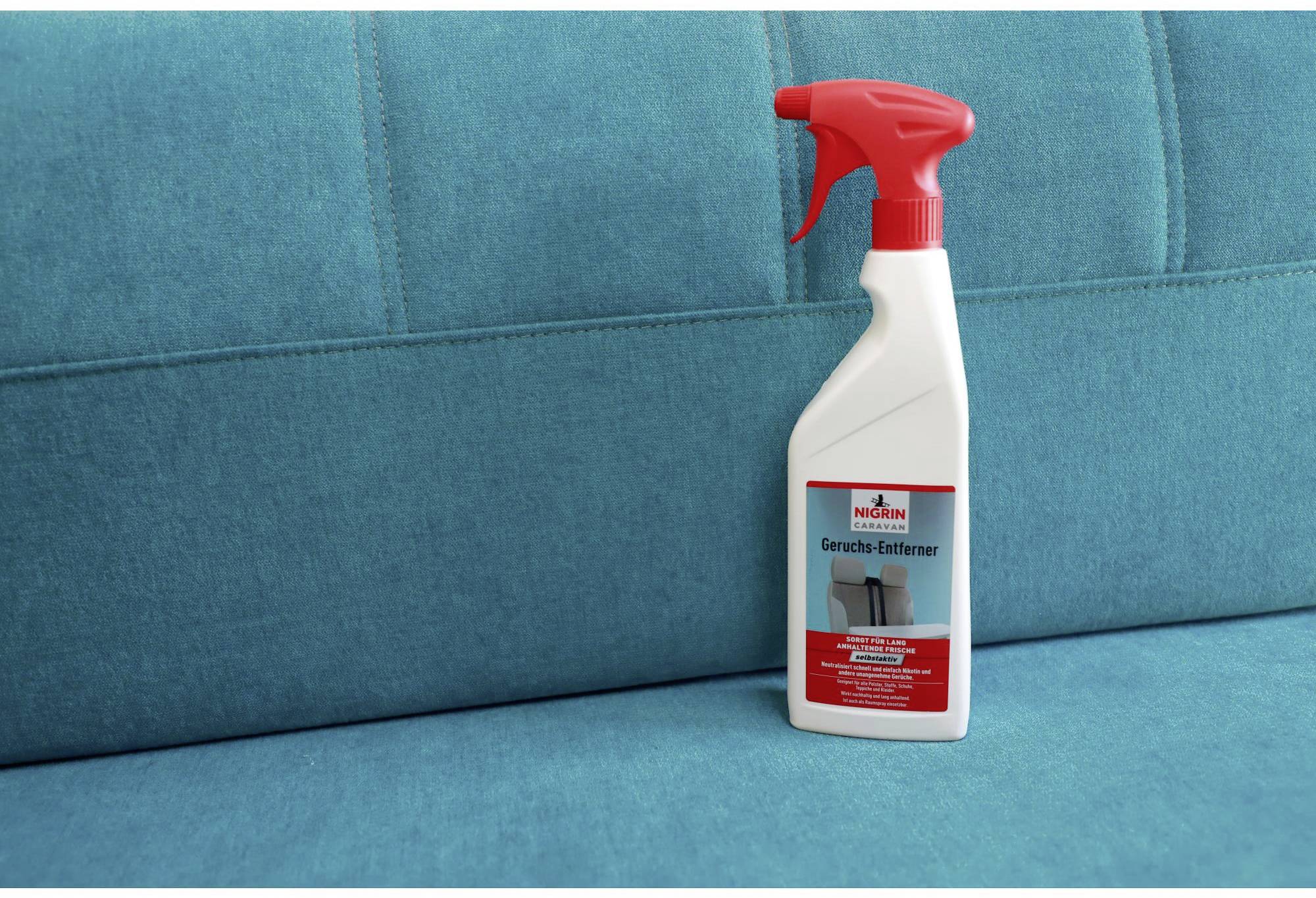 A red spray bottle of odour remover sits on a turquoise sofa.