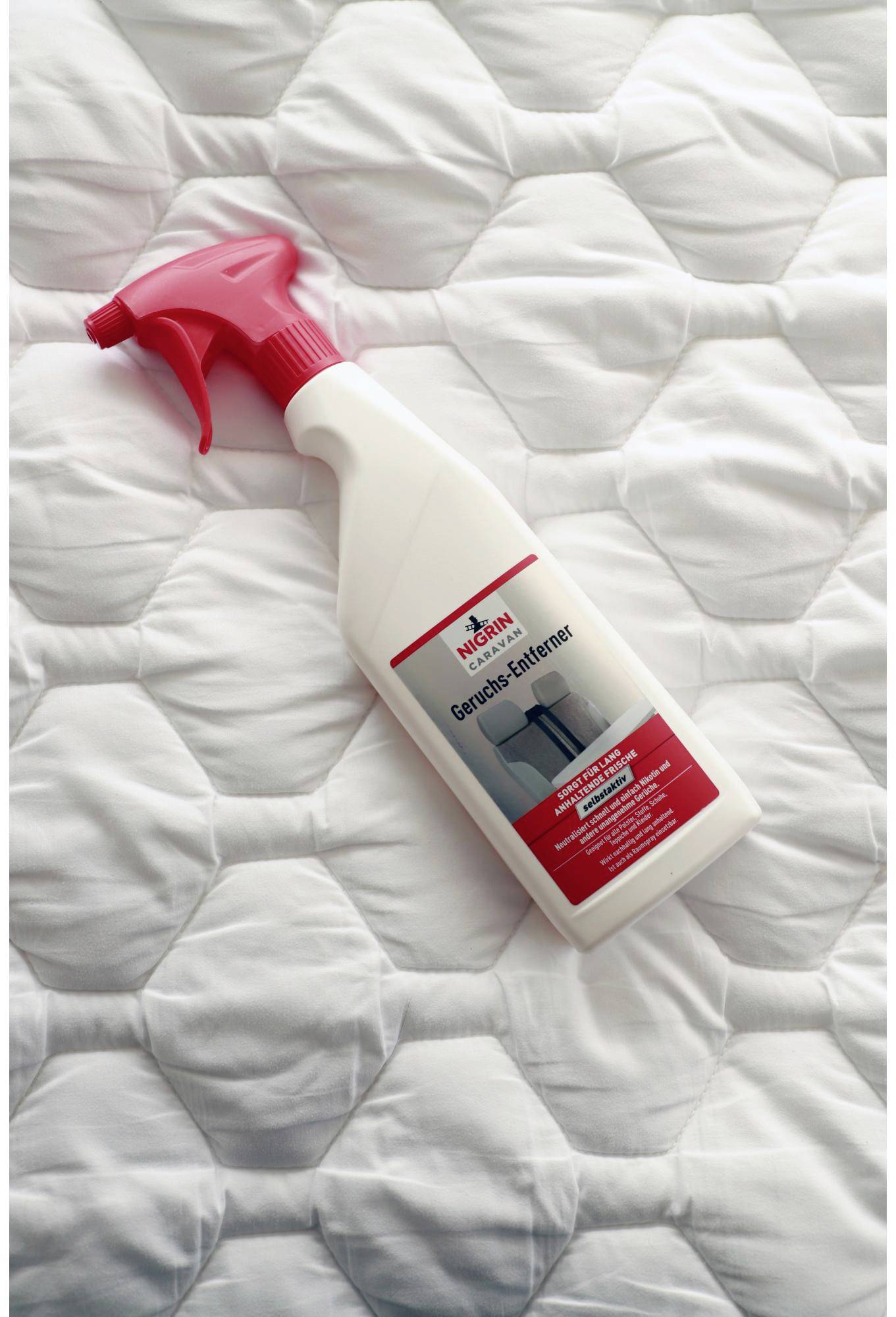 A bottle of curtain remover with a red spray nozzle lies on a white, quilted blanket.