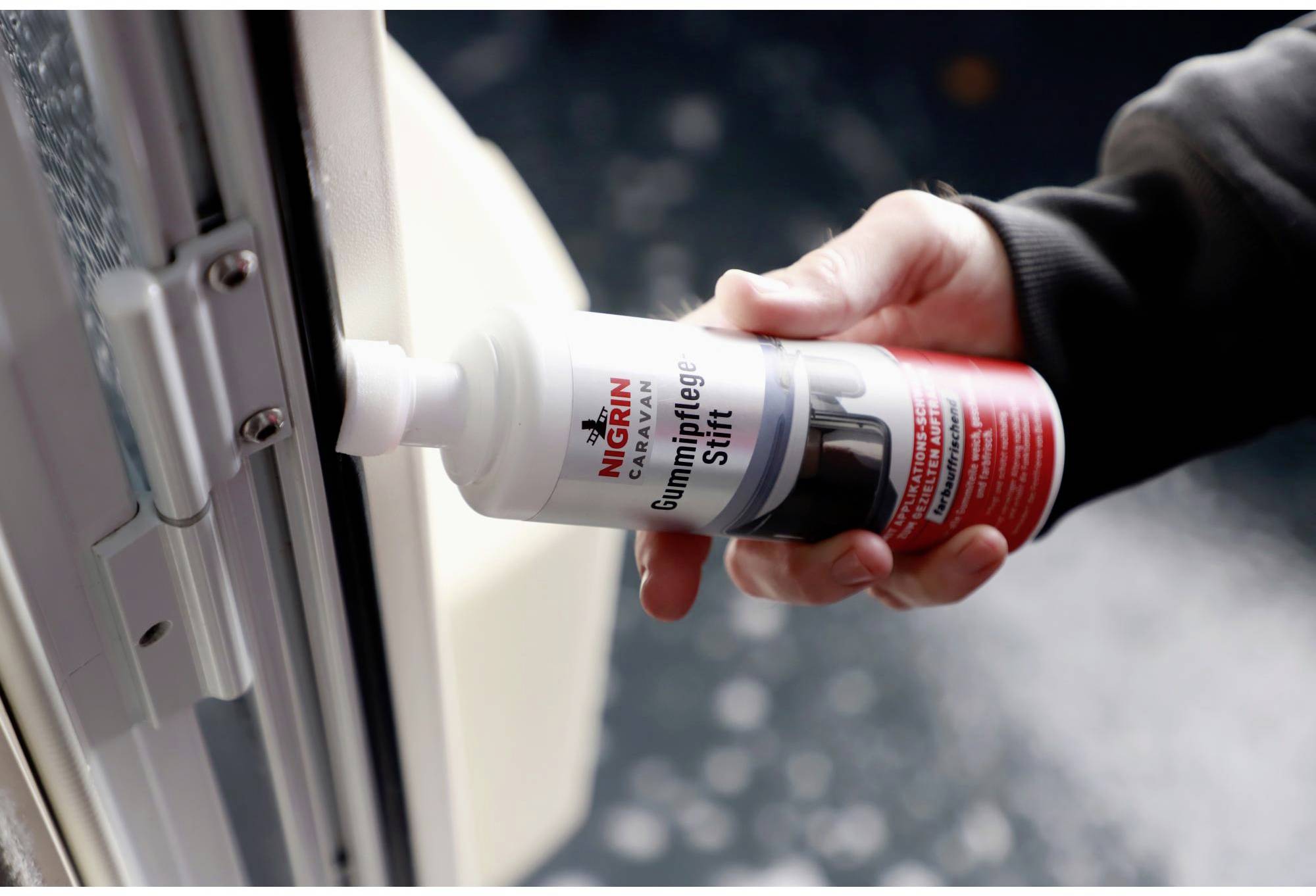 A person is holding a bottle of rubber care stick in their hand and applying care to the seal of a door.