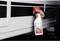 A hand is holding a white spray bottle with a red cap. The bottle is labelled 'Surface Sealing' and is being held against a white surface.