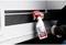 A person is spraying a cleaning solution from a white bottle with a red label and spray nozzle onto the surface of a vehicle.
