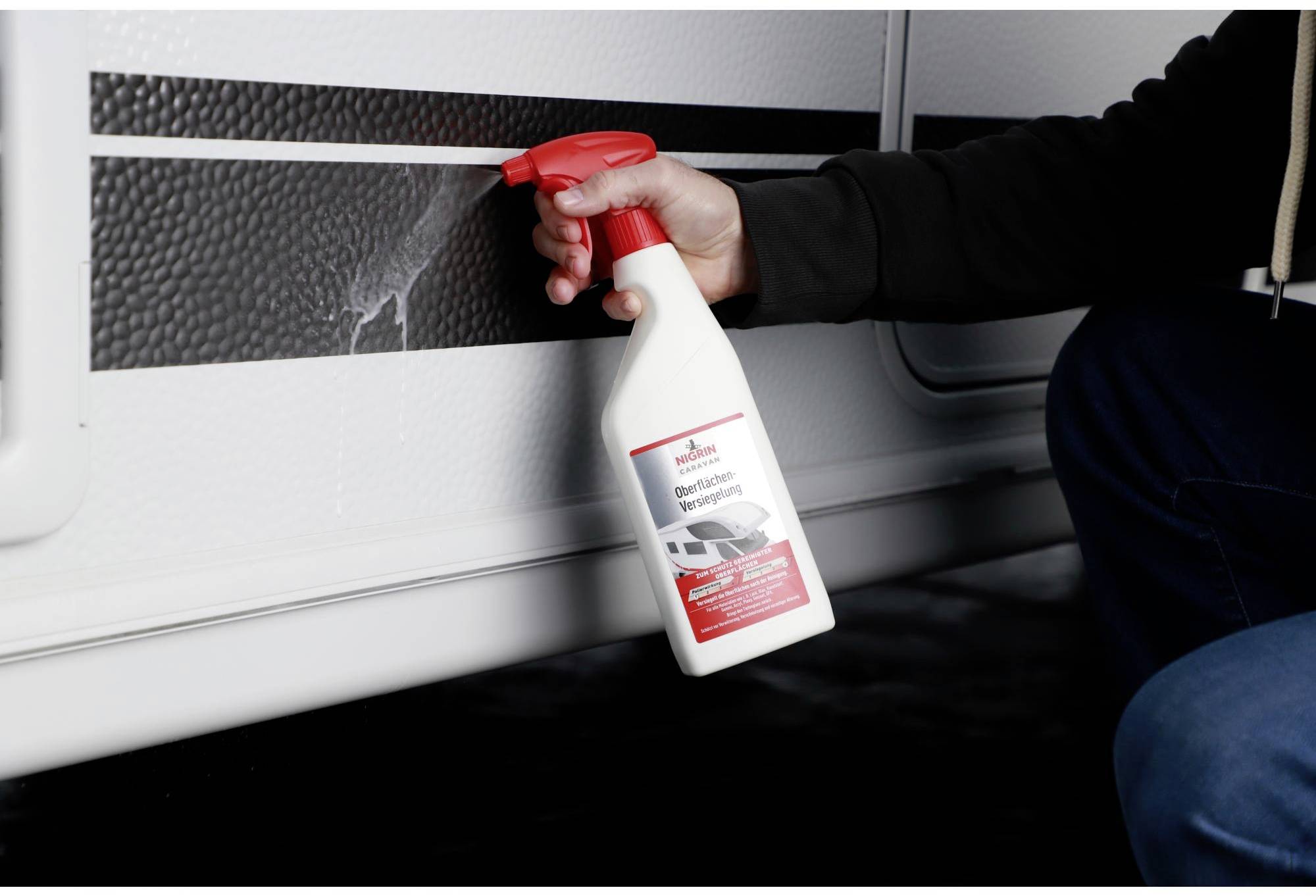 'Hand holding cleaning bottle and spraying on caravan surface.'