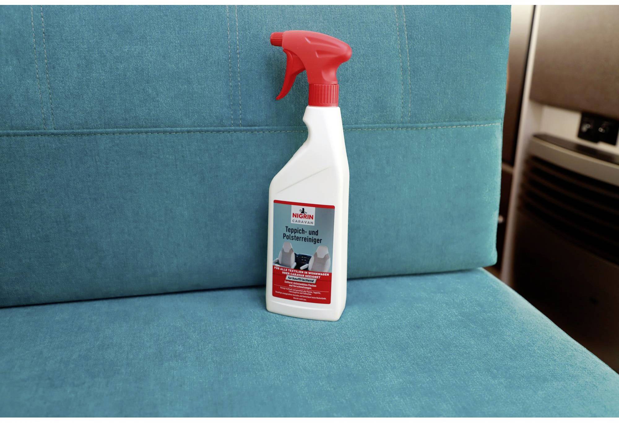 A bottle of carpet and upholstery cleaner sits on a turquoise sofa cushion. The bottle has a red spray nozzle.