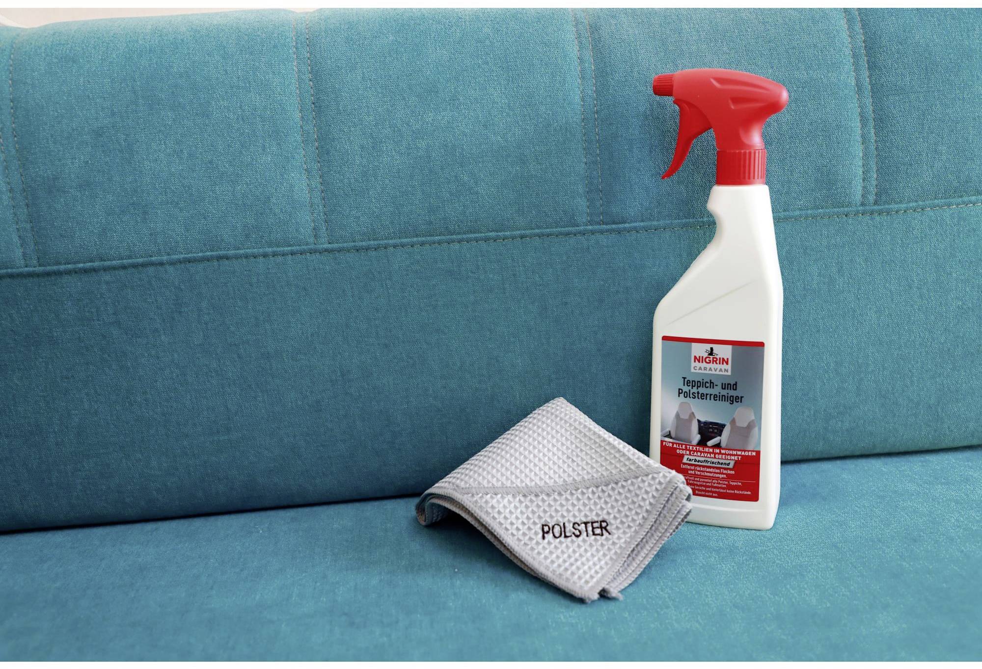 Turquoise sofa with a bottle of 'upholstery cleaner' and a grey cleaning cloth placed on top.