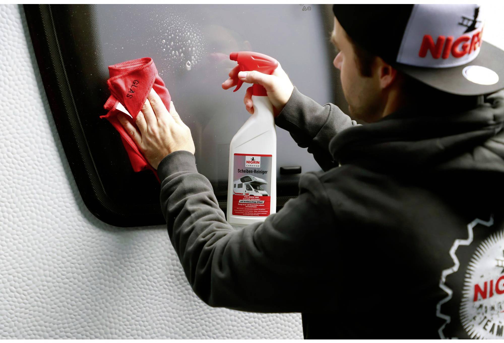 A person is cleaning a vehicle's window with a red cloth and a cleaning solution in a spray bottle.