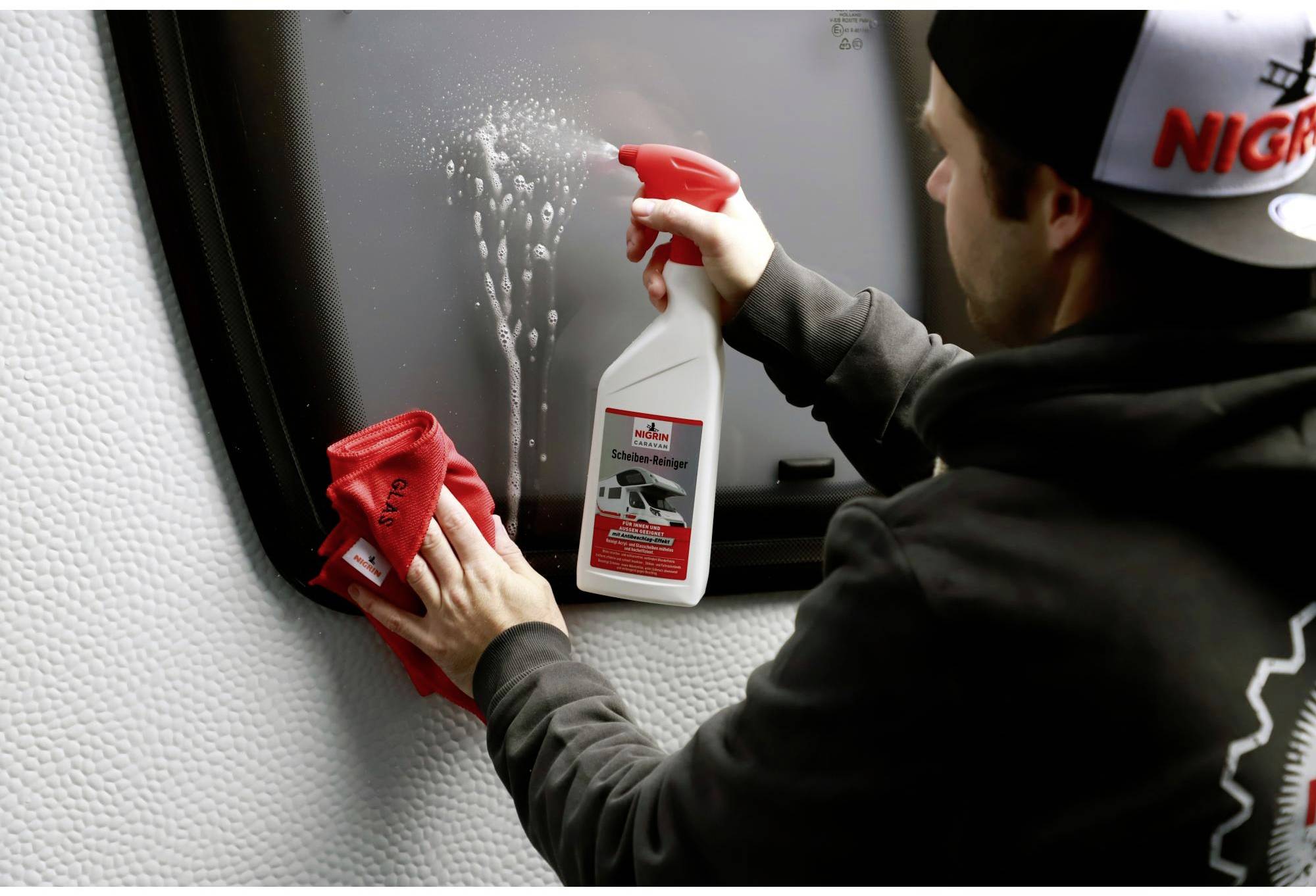 A man is cleaning a window with a red cloth and a spray.