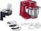 Red stand mixer with stainless steel bowl, various attachments and accessories including whisk, dough hook, food processor and grating discs.