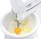 A mixing bowl with flour, small pieces of butter and an egg under an electric mixer.