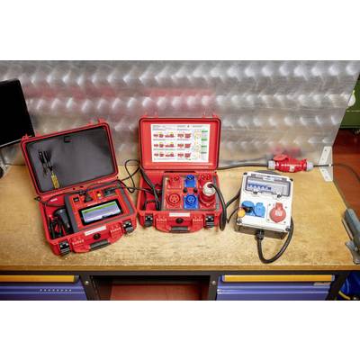 Red and grey electrical equipment on a workbench in a workshop, including measuring devices and junction boxes.