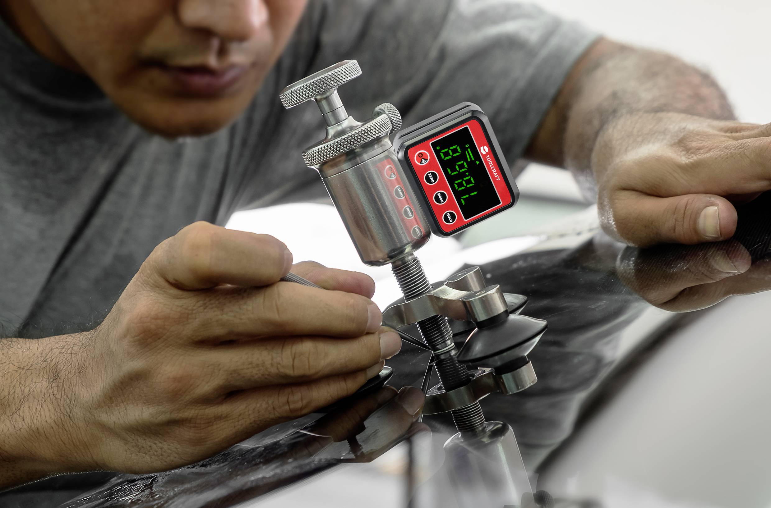 A person is working with a digital measuring instrument on a car part, possibly for inspection or repair.