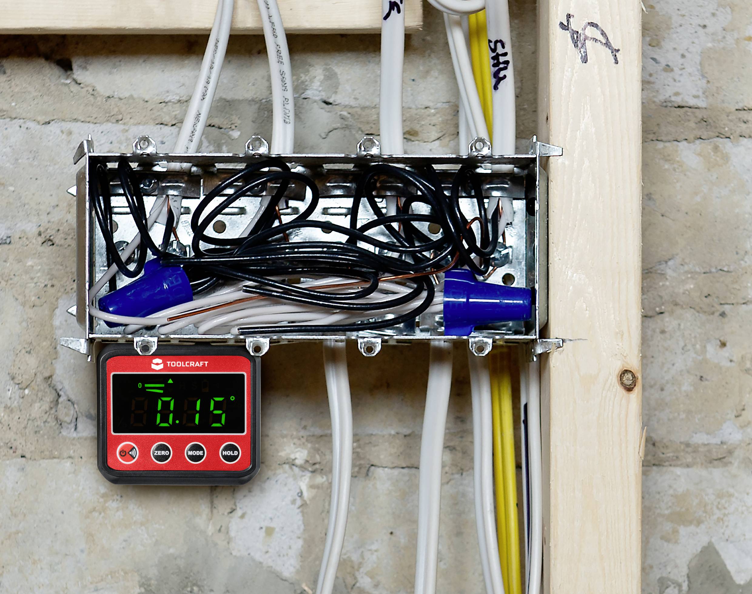 An open distribution box with cables and a digital measuring device displaying the value '0.15', mounted on a wall.