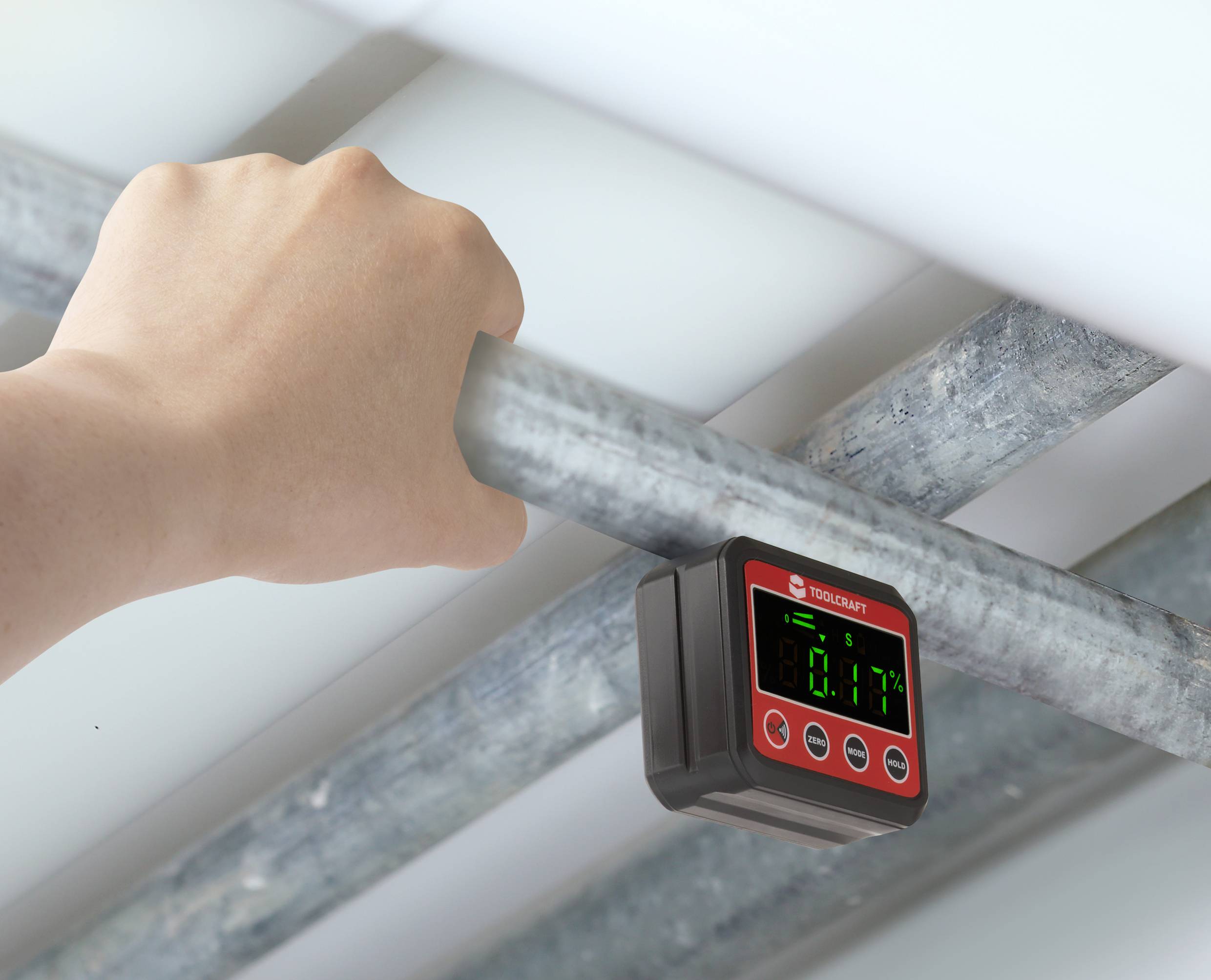 A hand is holding a metal pipe, with a digital measuring device attached underneath. The device displays a reading of '80.1' on a green display.