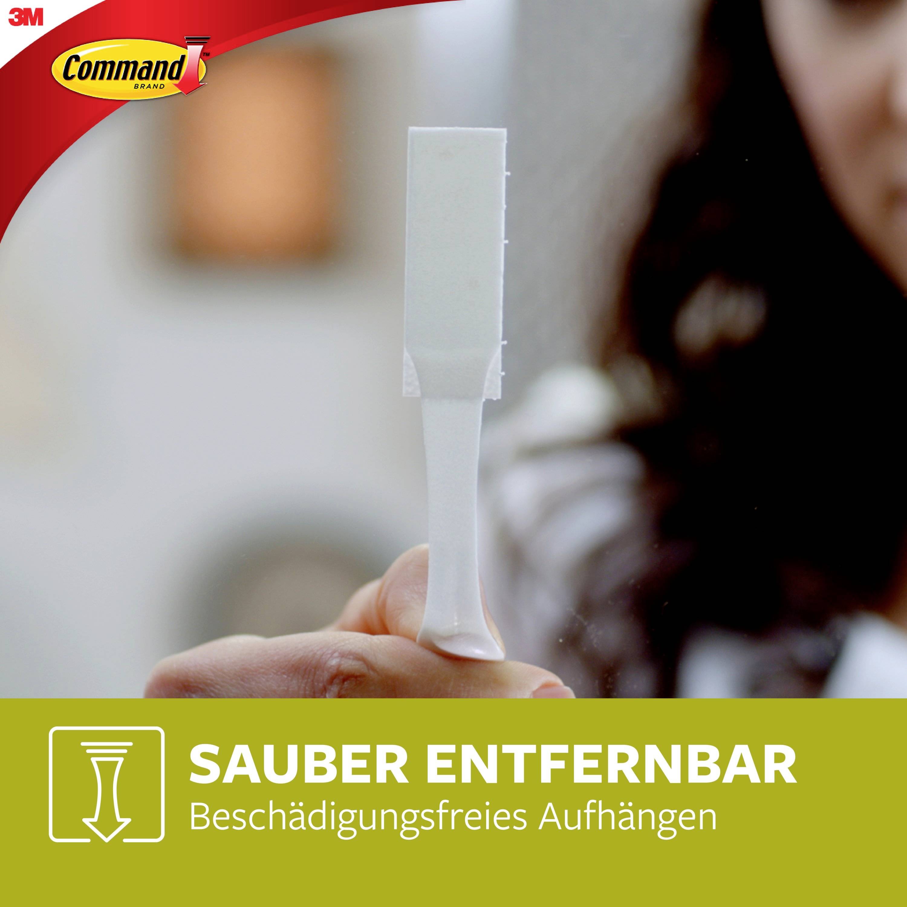 A person is holding a white hook remover in their hand. Text below: 'Cleanly removable, damage-free hanging'.