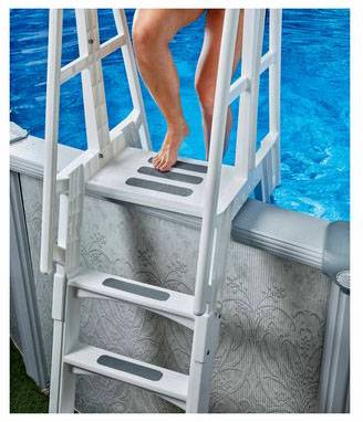 A person is descending a white ladder leading to an above-ground swimming pool.