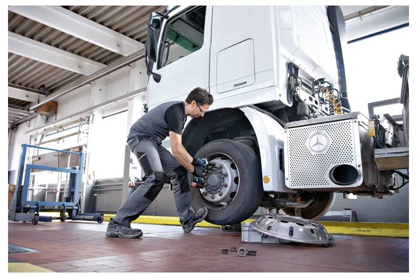 A mechanic in a workshop is fixing the wheel of a large truck elevated on a lift, showing a focus on vehicle maintenance and repair.