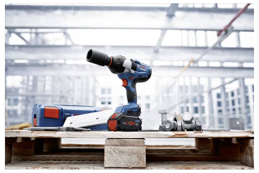 A cordless power drill on a wooden pallet at a construction site, surrounded by metal fittings, with metal framework visible in the background.