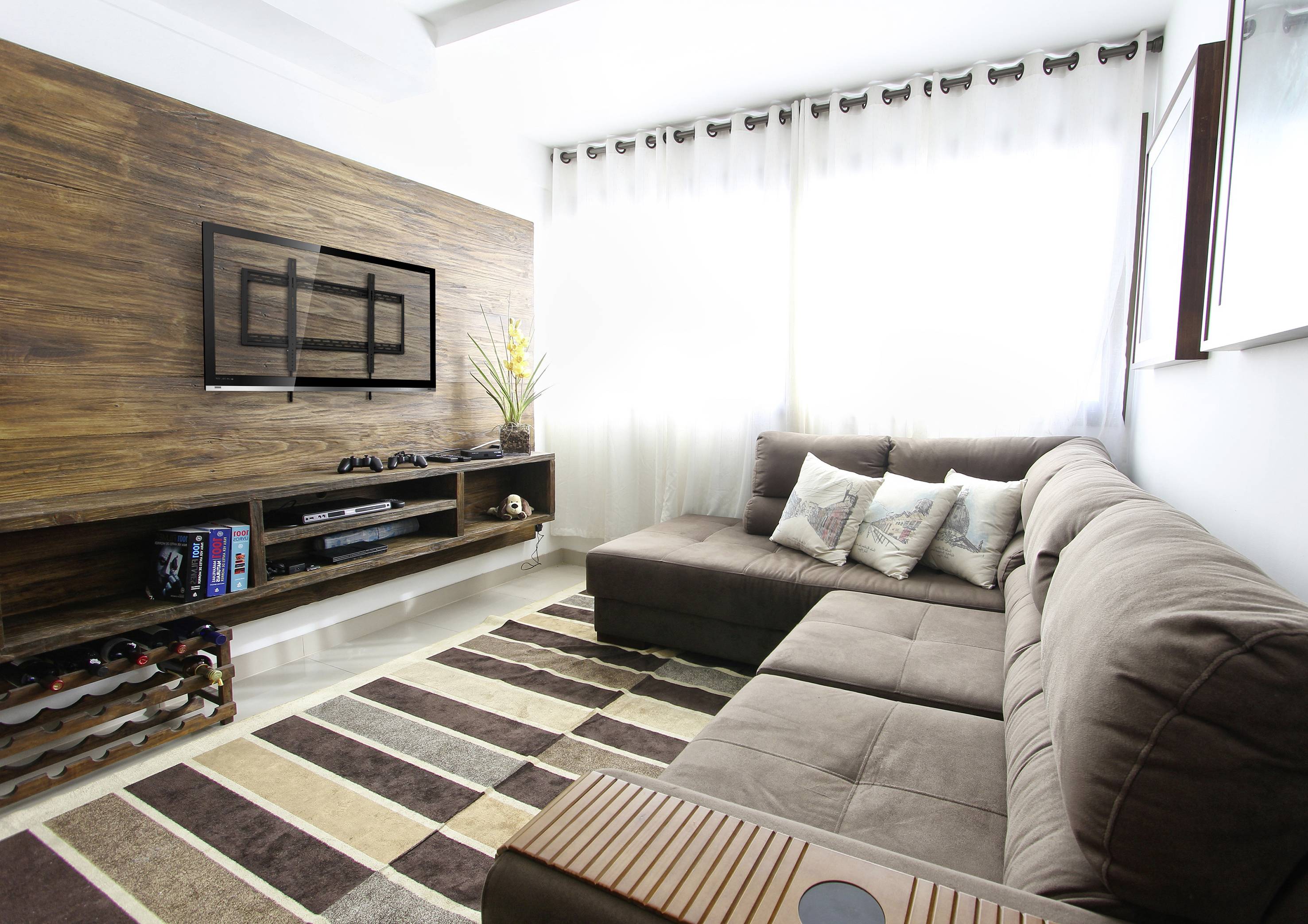 A modern living room with a brown sofa, striped rug and wall-mounted TV. Bright curtains allow sunlight to stream in.