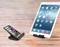 A smartphone and a tablet are sitting on a wooden surface, each in black stands. Both are displaying their home screens.