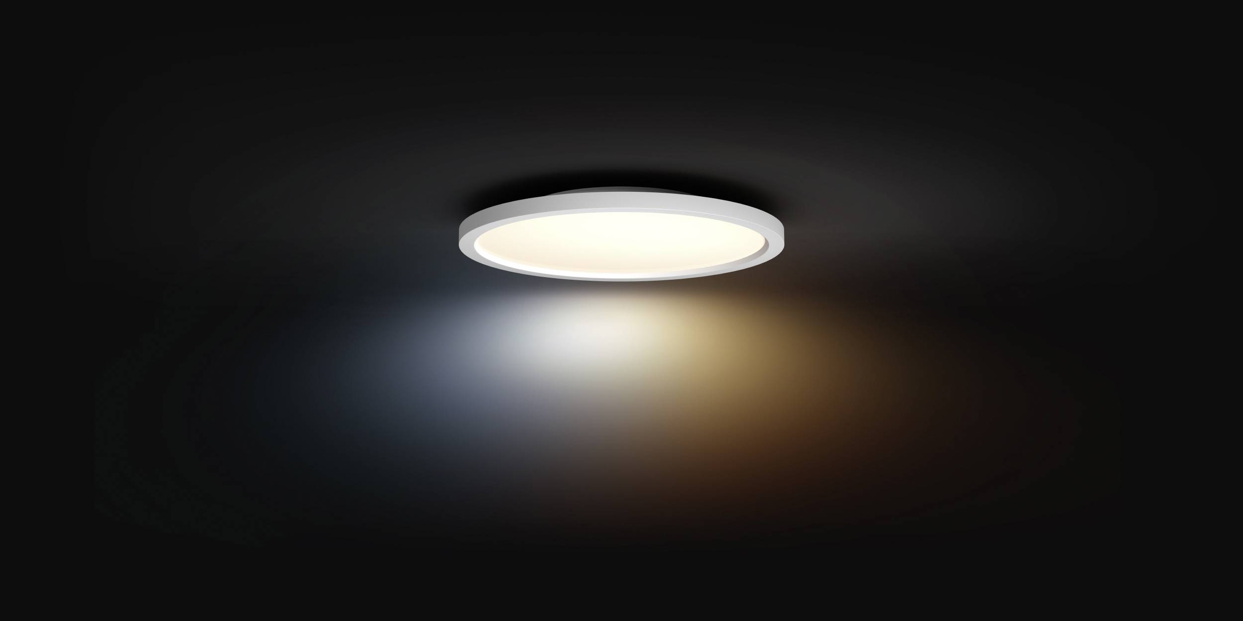 Circular ceiling light in the centre of a dark room, glowing in warm white and casting soft light rays across the ceiling surface.