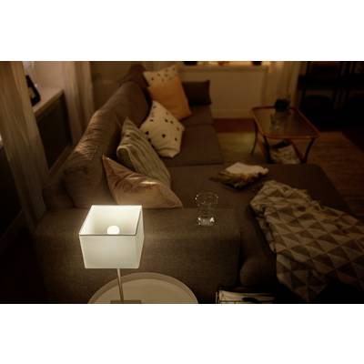 Cosy living room at dusk, sofa with cushions, a glowing lamp on a side table, throws and decorative elements.