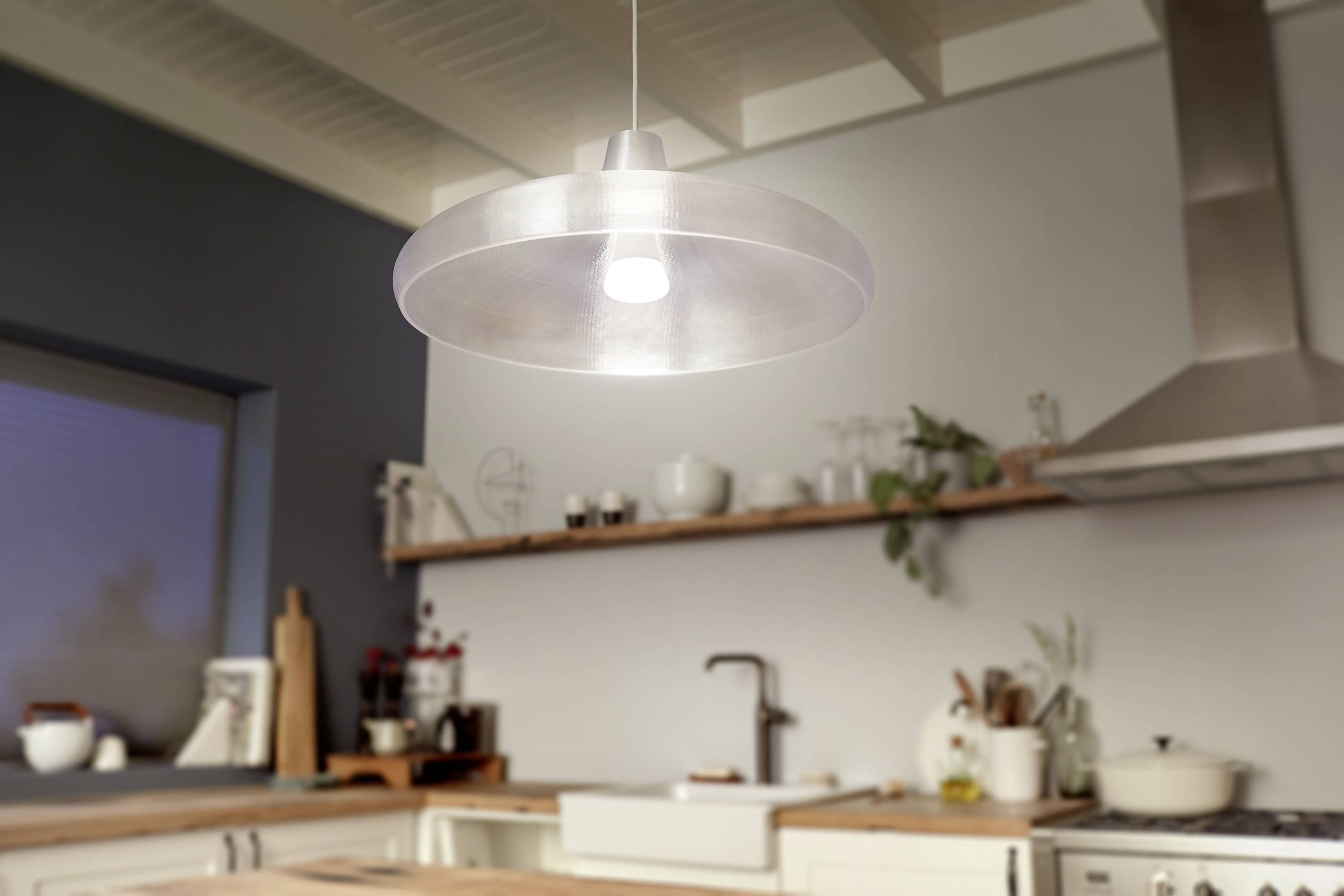 A stylish, modern kitchen with a suspended, round ceiling light above an island. Kitchen utensils and plants in the background.