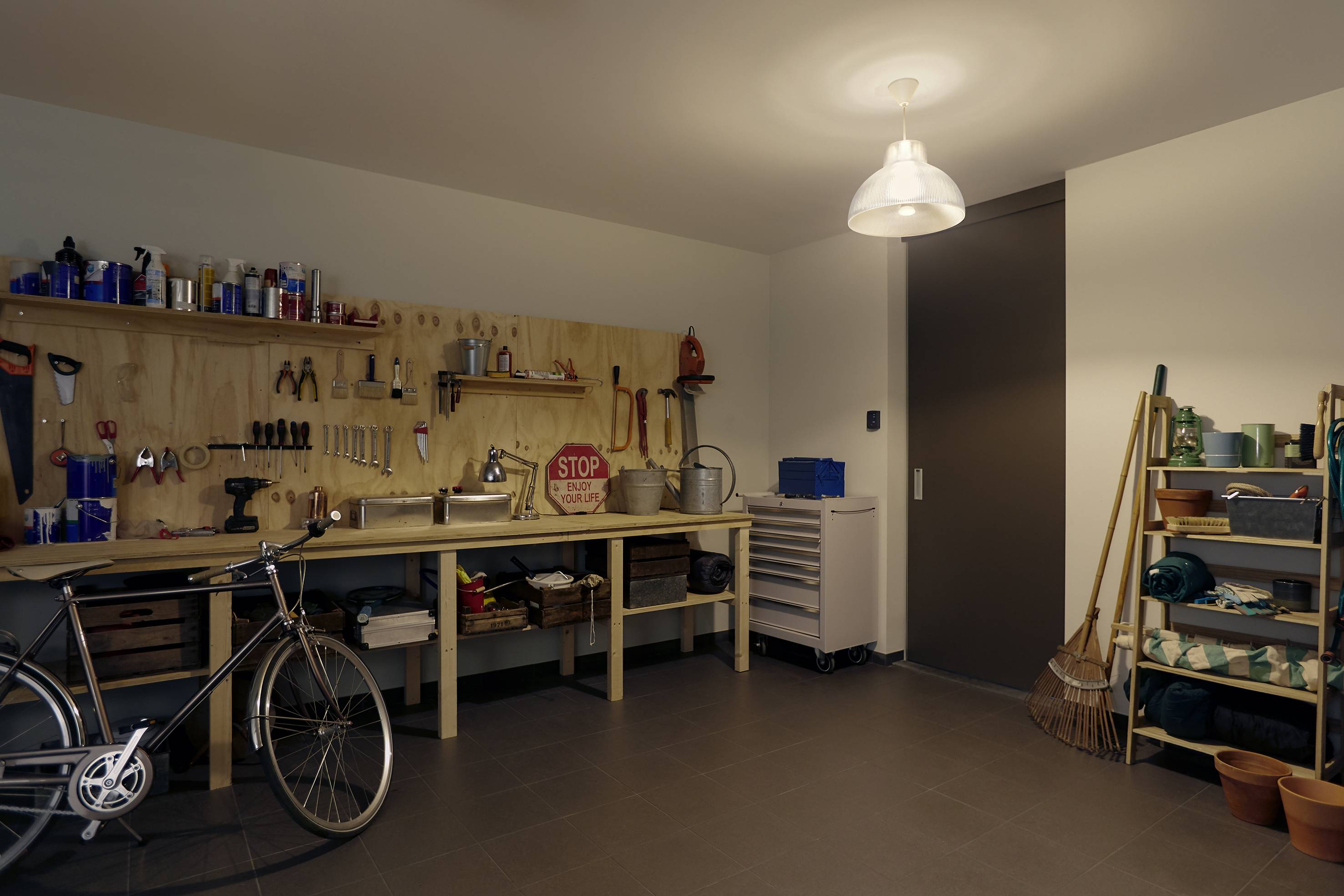 Bicycle in a workshop with tools on the wall, shelves of gardening equipment, and good lighting.