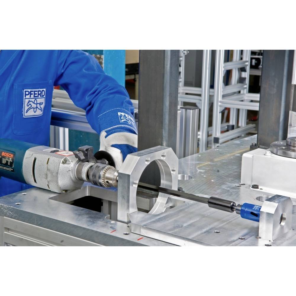 A drill secured in a metal construction. An employee in blue workwear is carrying out precise work.