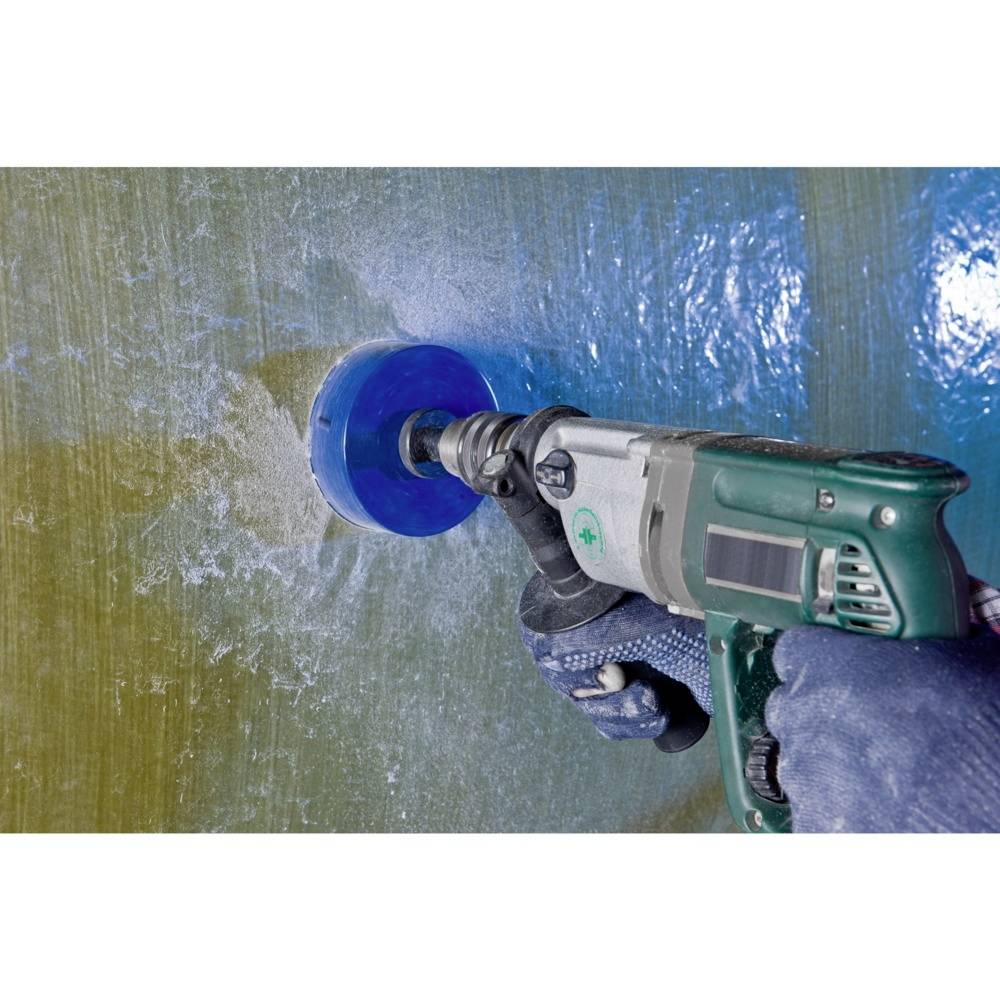 A hand is holding a drill with a blue drill bit, boring a round hole into a fibreglass-reinforced surface.