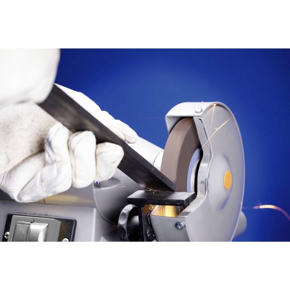 A person wearing white gloves is grinding a piece of metal on a stationary grinding machine, with sparks flying into the air.