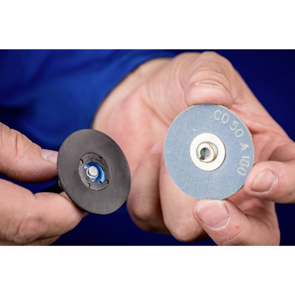 A person is holding two grinding discs of different types in their hands; on the left a black one, on the right a blue one with the inscription 'CD 50 A 180'.