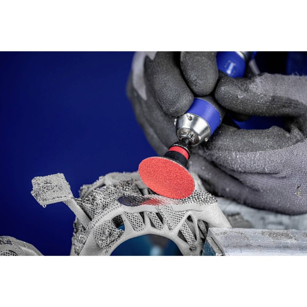 A gloved hand is using a grinding tool to smooth the surface of a complex metal component.