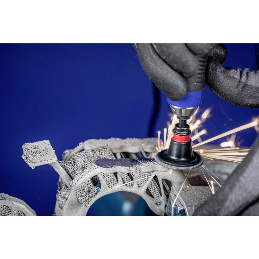 A person is machining a complex, metallic component with a rotating tool. Sparks are flying in all directions.