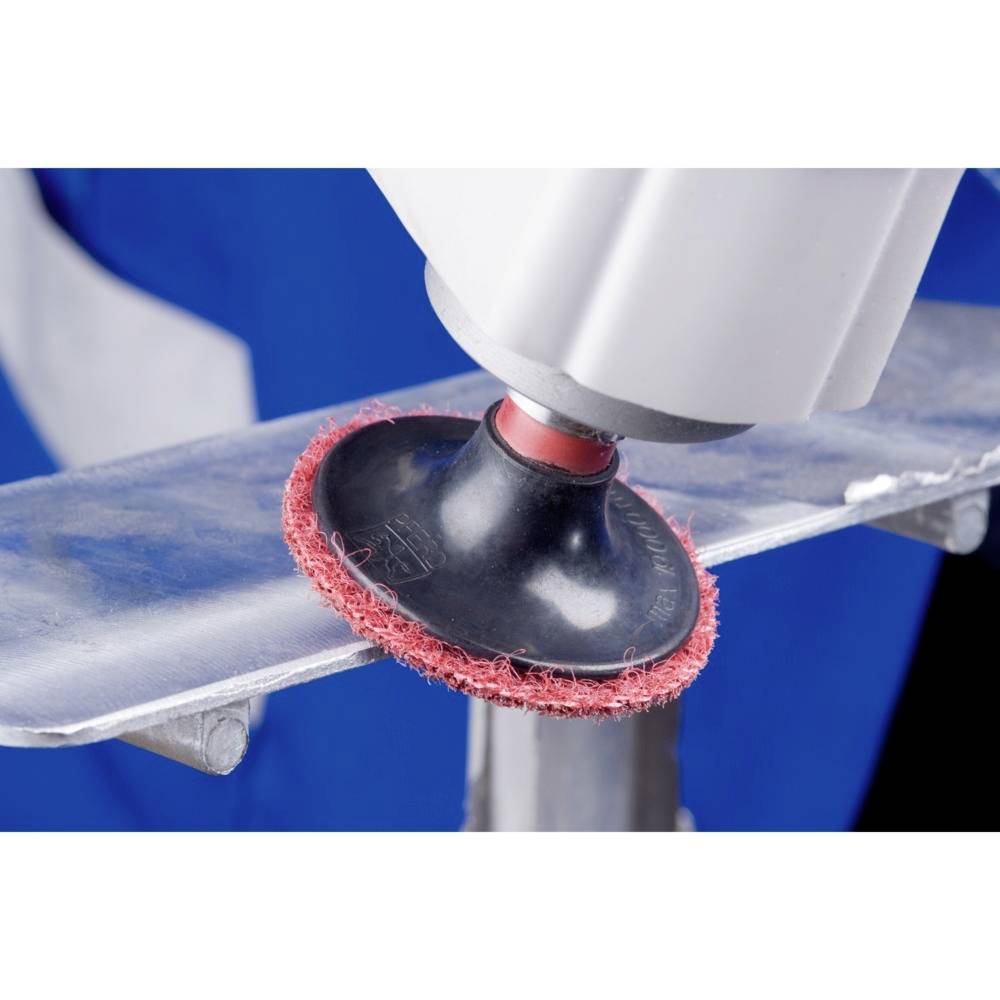 A polishing device with a red polishing attachment is working on a metal surface. In the blurred background, a person in workwear is visible.
