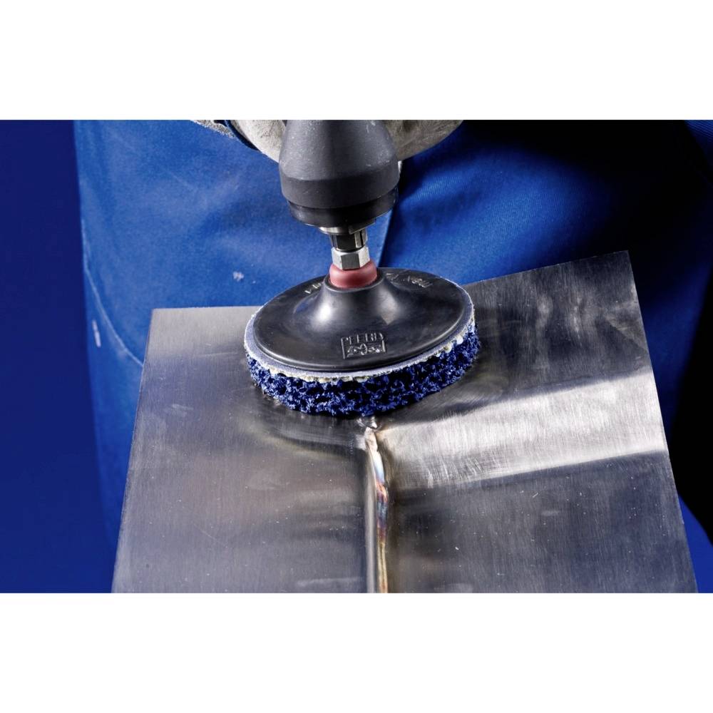 A person is working with a polishing machine to smooth a metallic surface. The person is wearing blue workwear.