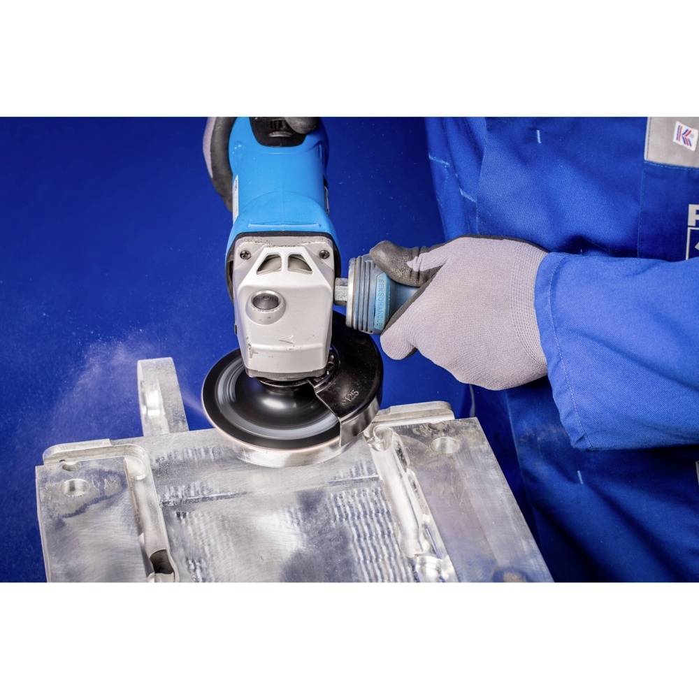 A person in blue workwear is polishing a metal piece with a grinding machine. The scene emphasises precision work and craftsmanship.