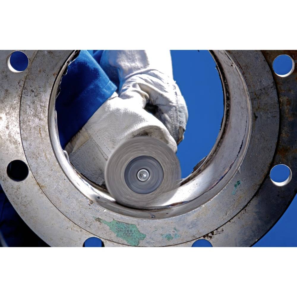 Worker in protective clothing grinds metal part with a rotating machine. Concentrated focus on the grinding process.