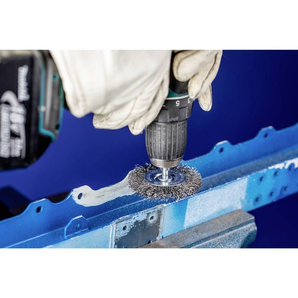 A person is grinding a blue metal frame with an attachment on a cordless drill to remove paint.