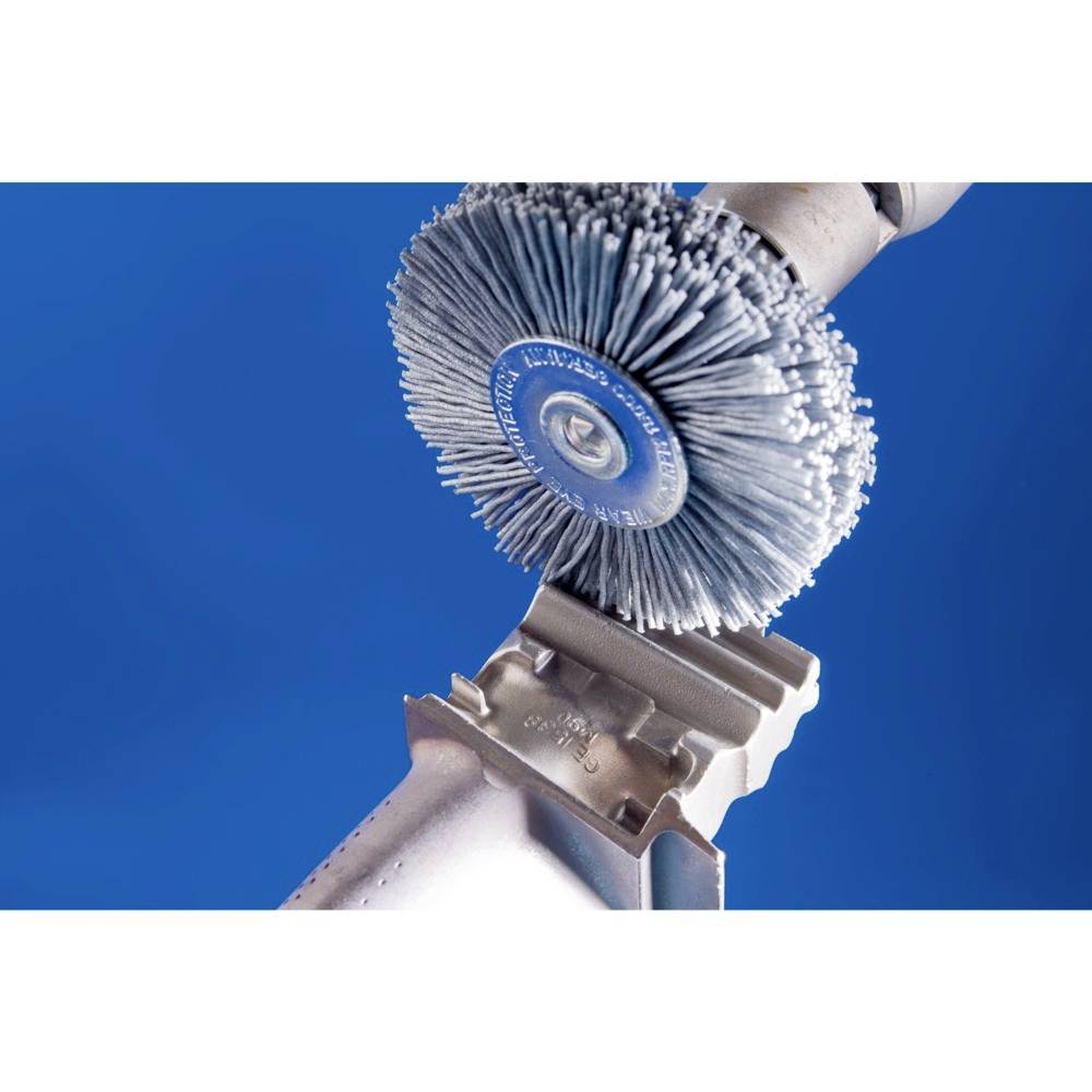 A metal part is being processed by a rotating wire brush, against a blue background. The scene depicts a polishing process.